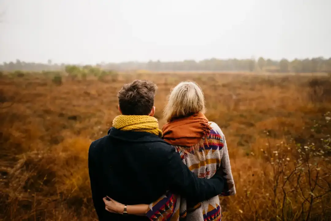 Dos personas se abrazan de lado en un campo, al atardecer.