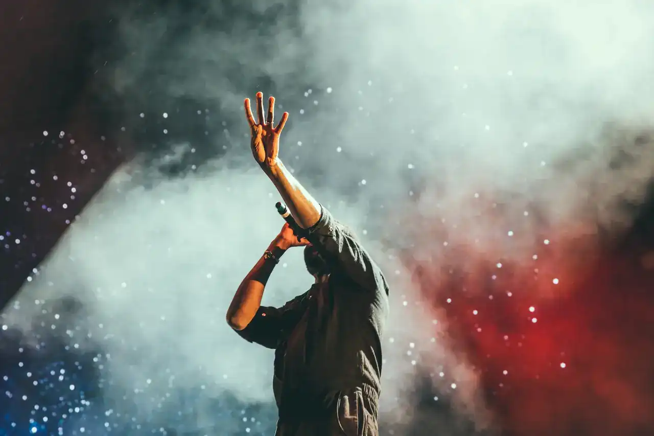 Un cantante levanta la mano en la tarima entre humo y luces.