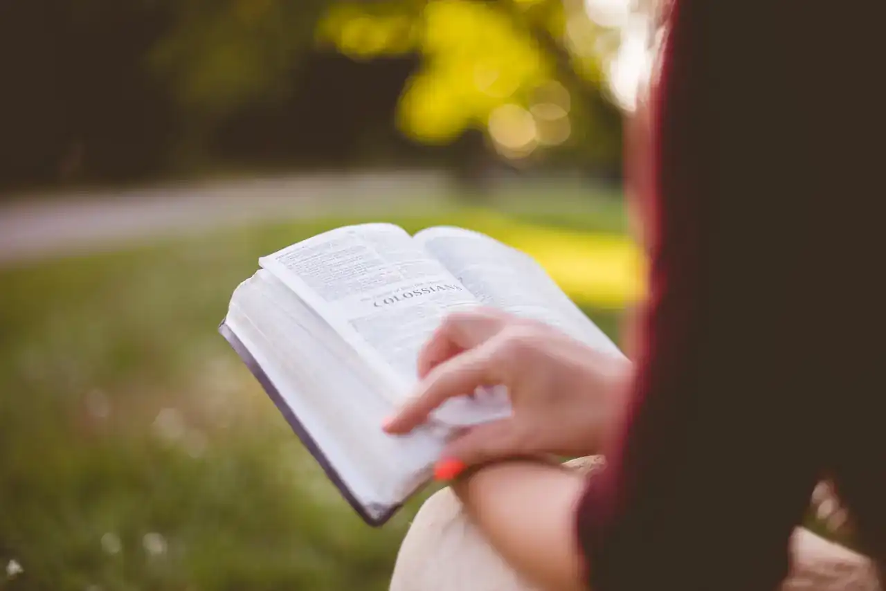 Una persona lee una Biblia abierta sentada en el pasto.