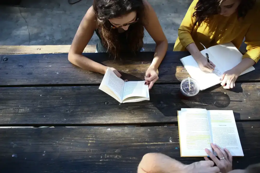 Dos personas leen y toman notas en una mesa de madera.