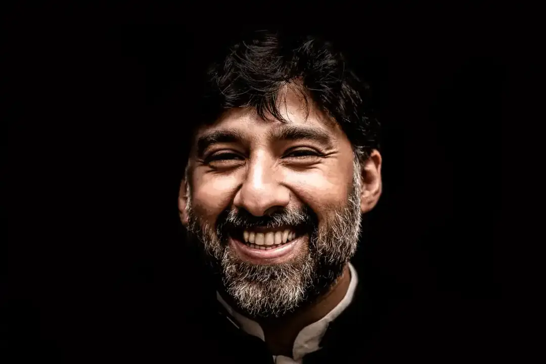 Retrato de un hombre sonriente de barba, sobre fondo oscuro.